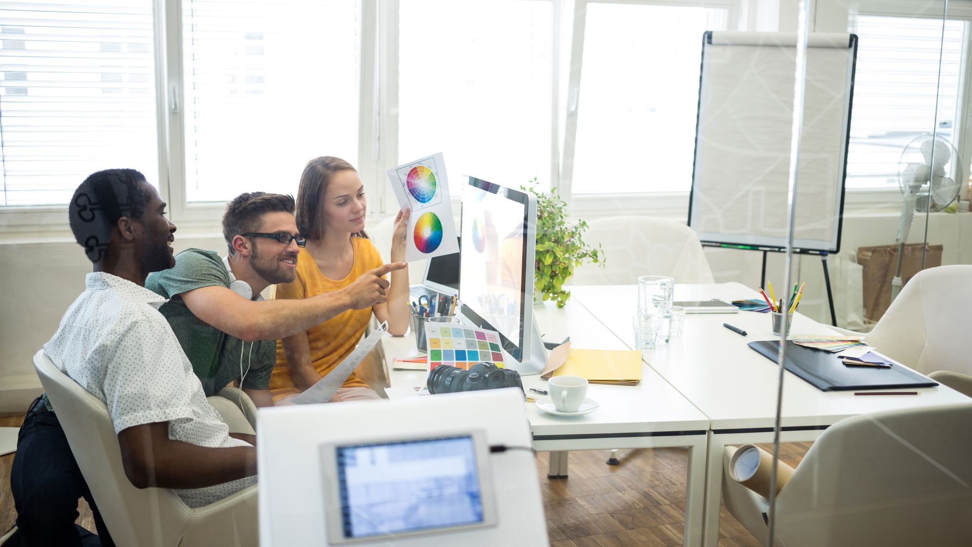Gruppo di designer al lavoro su monitor e materiali grafici per servizi digitali e comunicazione visiva